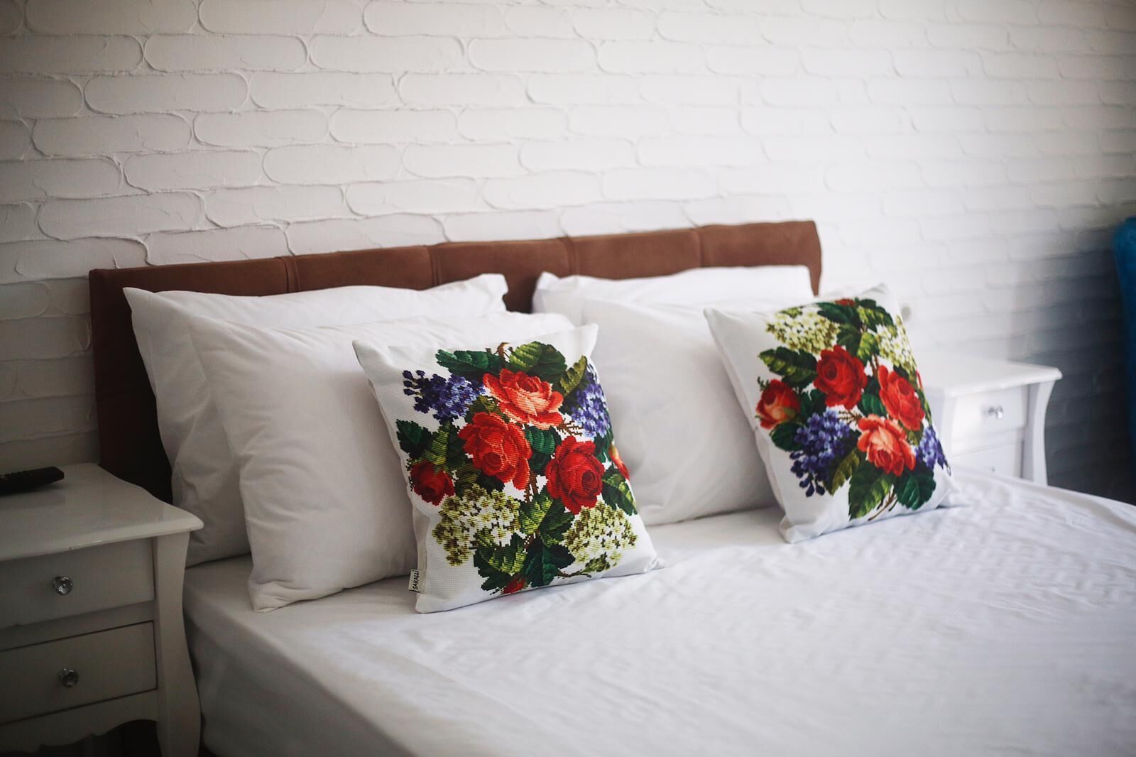A bed with white bedding and two decorative pillows with floral designs.