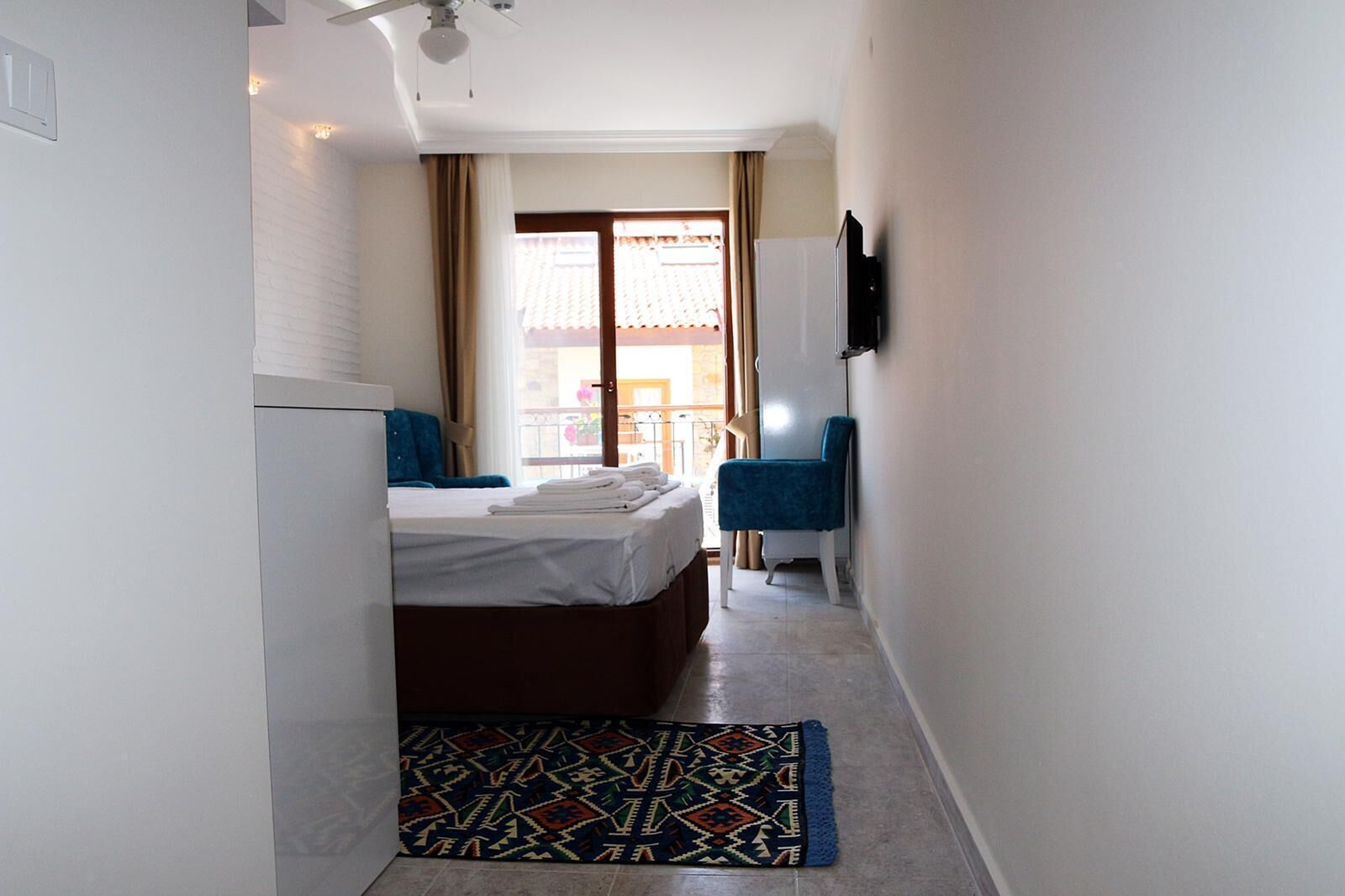 Un pasillo estrecho que conduce a un dormitorio con una cama, una silla y un televisor montado en la pared.