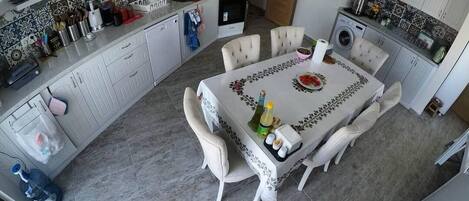 A kitchen with a dining area, featuring a tiled backsplash, white cabinets, and a central island with a sink and stove.