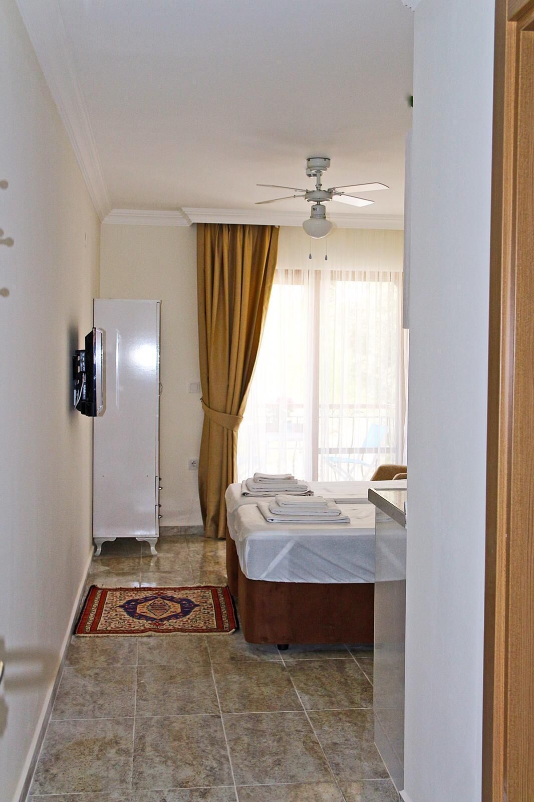 Una habitación de hotel con cama, ventilador de techo, refrigerador blanco y baño con espejo.