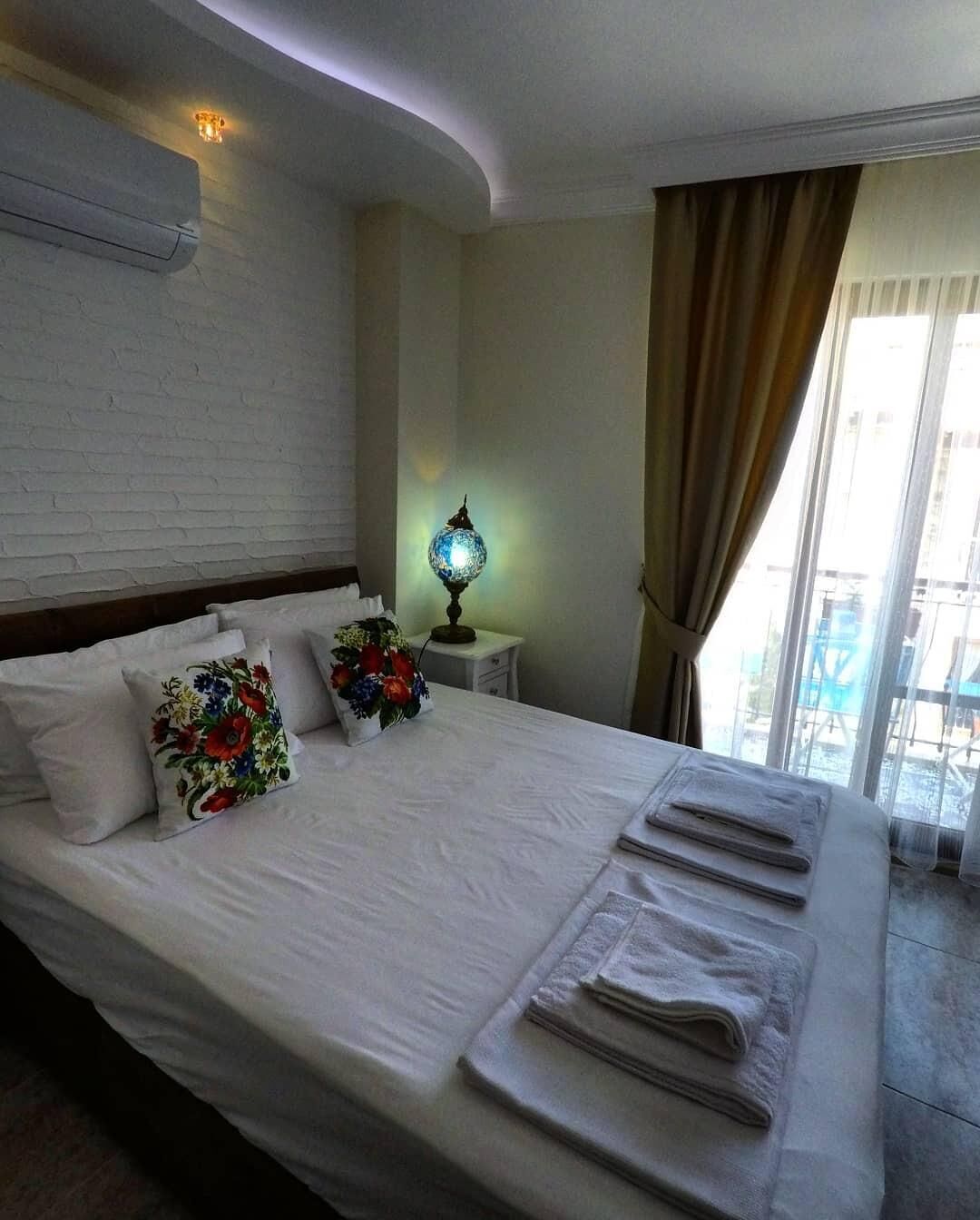 A hotel room with a neatly made bed, a lamp, and a view of the outdoors.