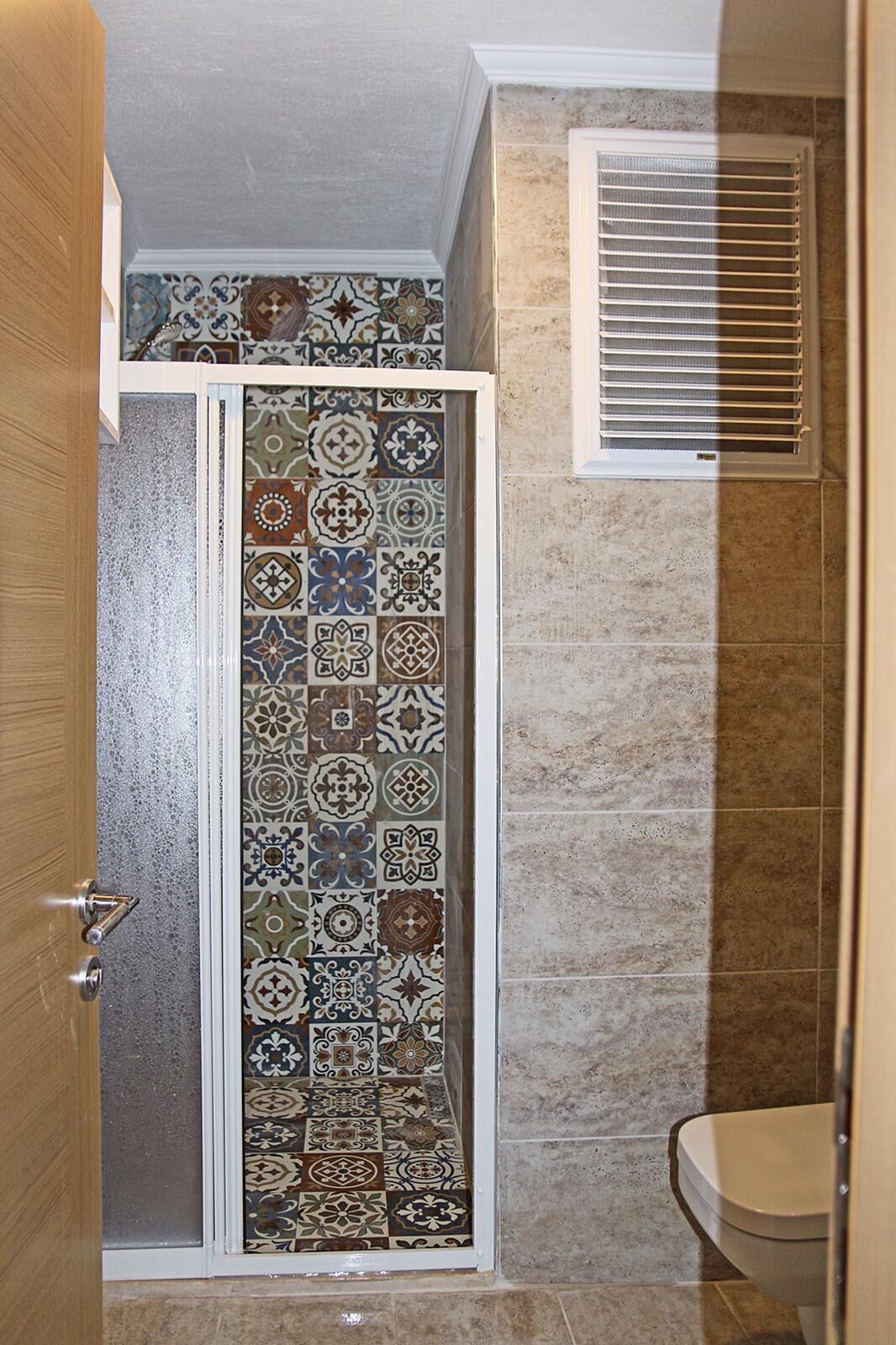 A bathroom with a shower area featuring a tiled wall with a variety of patterns.