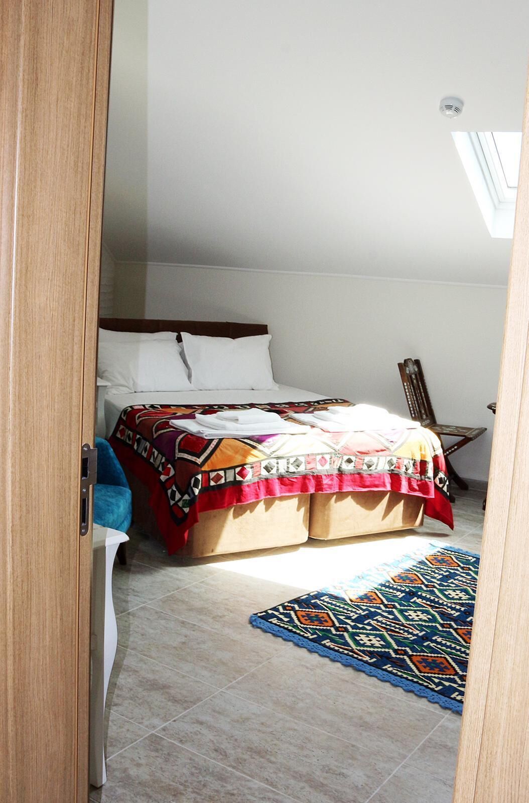 A bedroom with a bed, a chair, a small table, and a colorful rug.