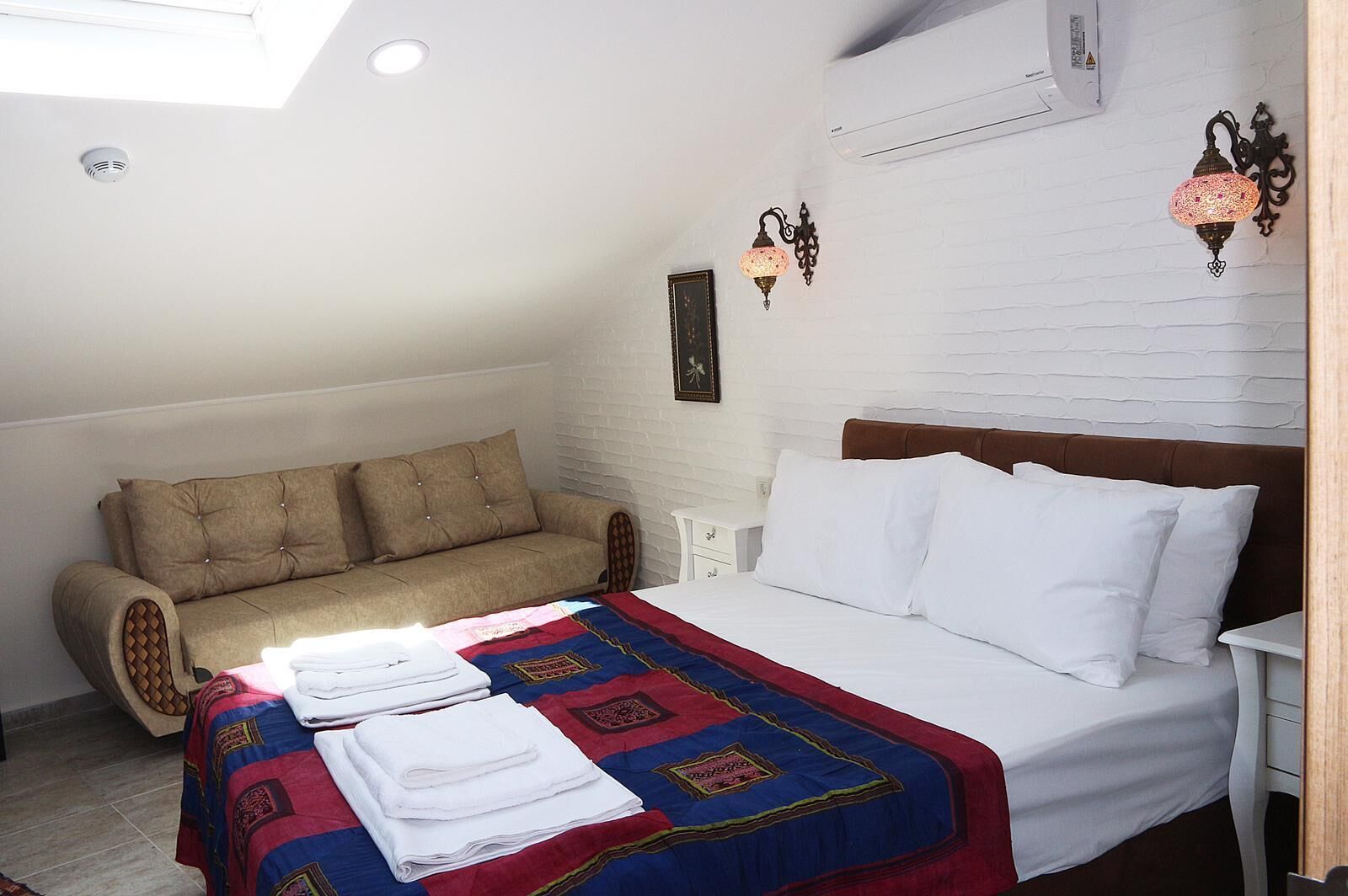 Quarto com cama, sofá, mesa de cabeceira e ar-condicionado fixado na parede.