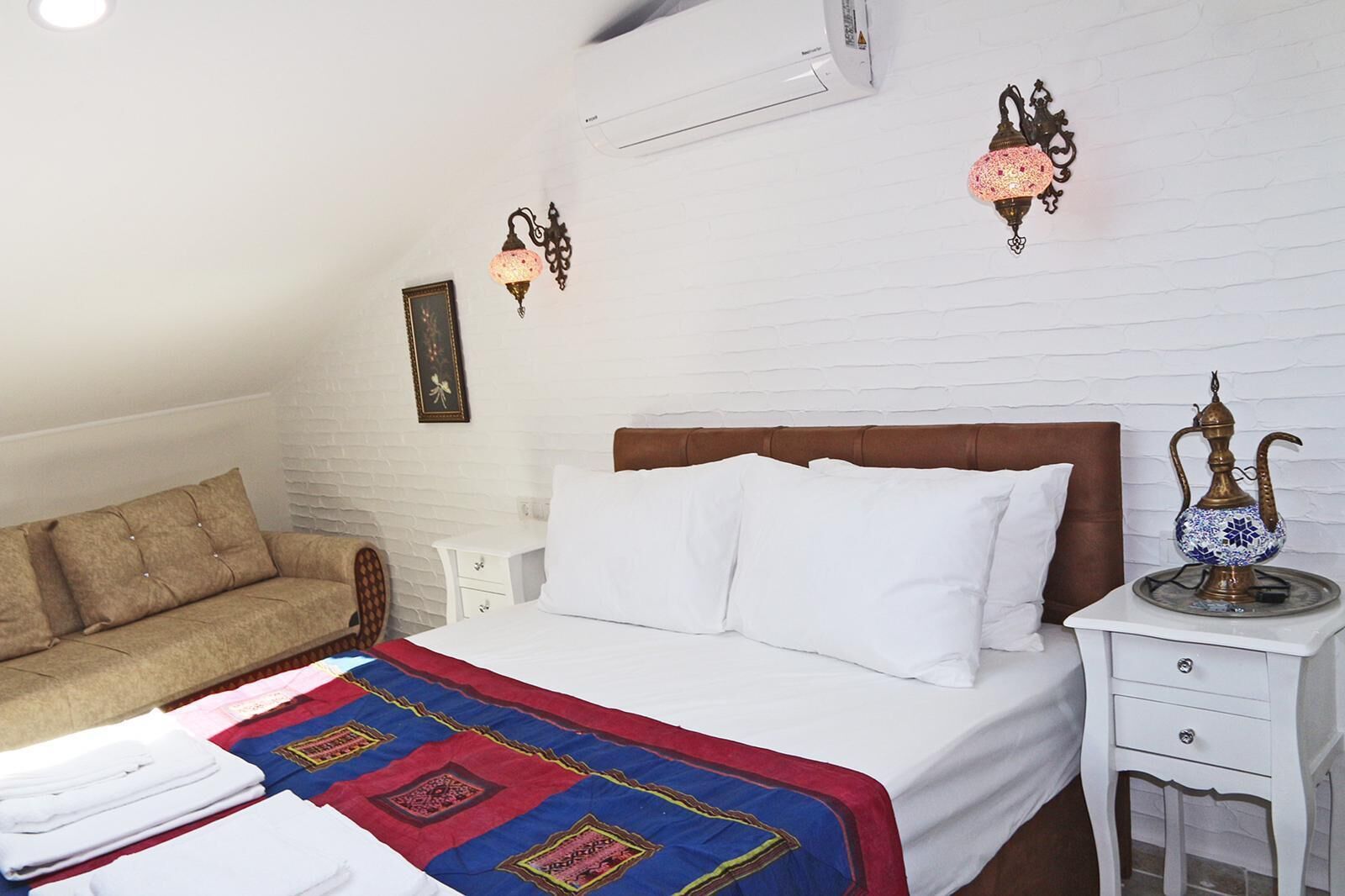 Een keurig opgemaakt slaapkamer met een bed, een bank, een nachtkastje en een decoratieve lamp.