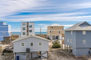 Una propiedad frente a la playa con varias construcciones, incluyendo una casa de dos pisos con balcón y una casa más pequeña sobre pilotes.