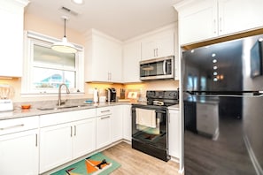 A modern kitchen with white cabinets, a stainless steel refrigerator, a microwave, and an oven. - Beachside Bungalow - Dog Friendly - Amazing views from rooftop deck! (Topsail Beach)