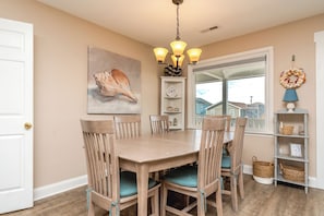 A dining area with a wooden table and chairs, a wall clock, and a large window. - Beachside Bungalow - Dog Friendly - Amazing views from rooftop deck! (Topsail Beach)