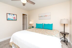 A bedroom with a bed, a door, a lamp, and a painting on the wall. - Beachside Bungalow - Dog Friendly - Amazing views from rooftop deck! (Topsail Beach)