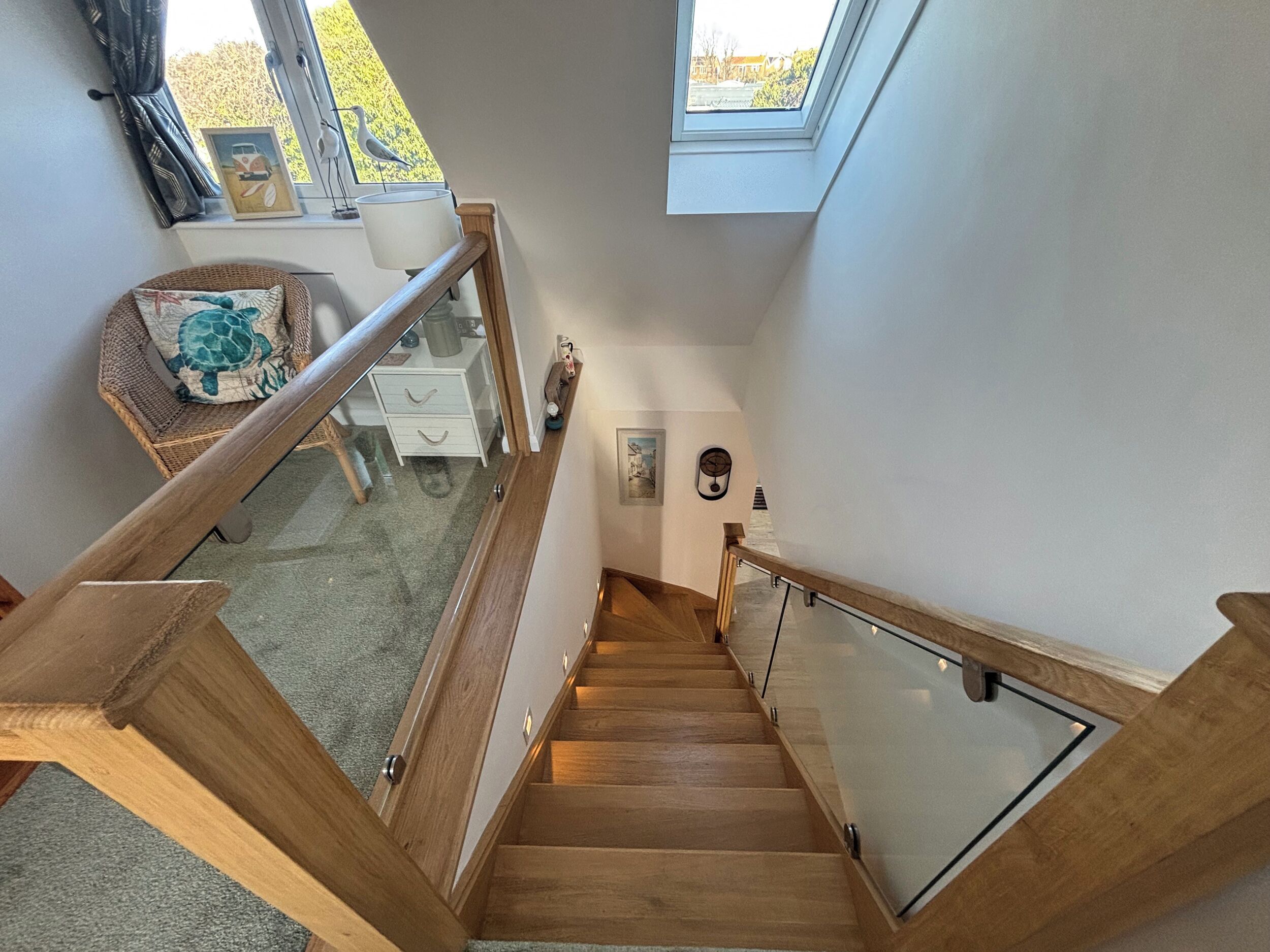 A wooden staircase with glass railings leading to a landing area with a chair and a small table.