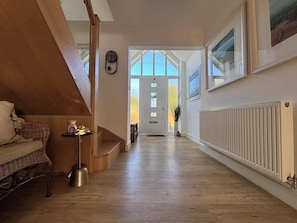 A hallway with a wooden floor, a wicker sofa, a small table with a lamp, and a radiator. - Seaview (Lowestoft)