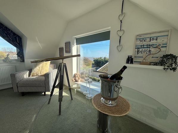 A cozy living room with a striped sofa, a telescope, a telescope stand, a bottle of champagne, and a 'see you at the beach' sign. - Seaview (Lowestoft)