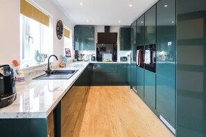 A modern kitchen with a marble countertop, wooden flooring, and a built-in oven. - Seaview (Lowestoft)
