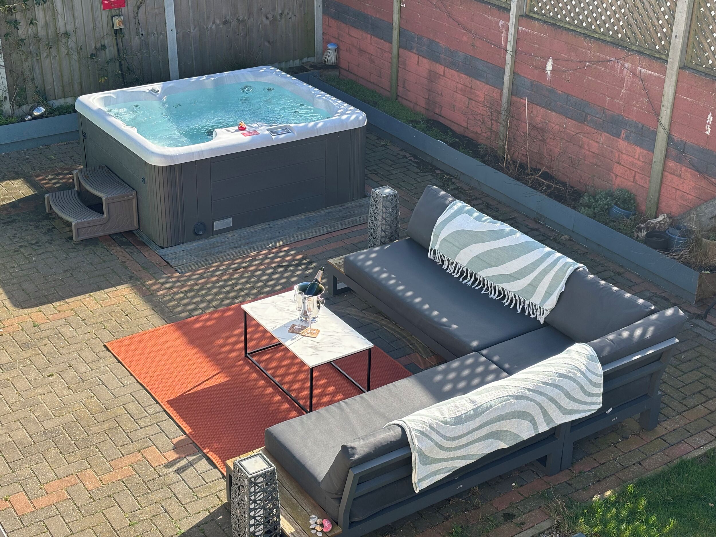 Ein Whirlpool, ein graues Sofa mit einem gestreiften Überwurf und ein kleiner Tisch mit einer Flasche und Gläsern.