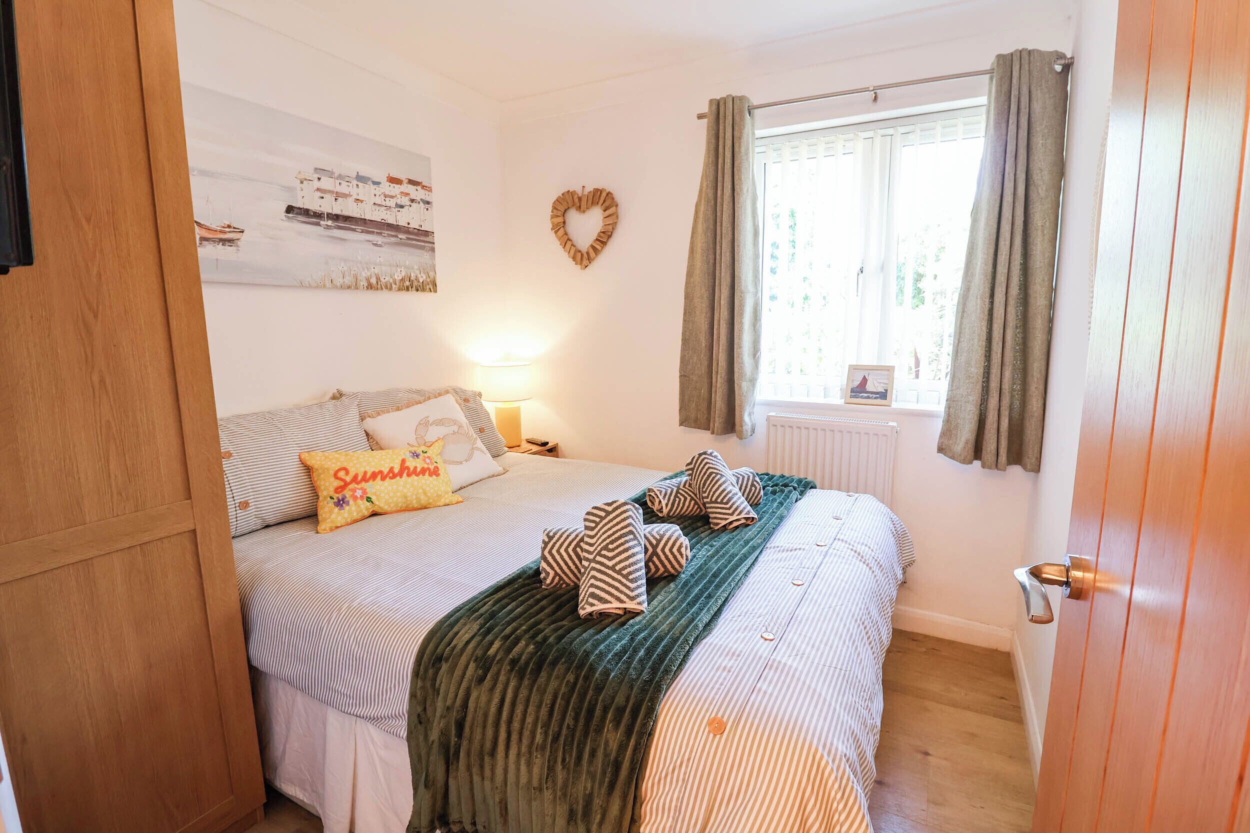 A bedroom with a bed, a bedside table, a lamp, a window with curtains, and a wall decoration.