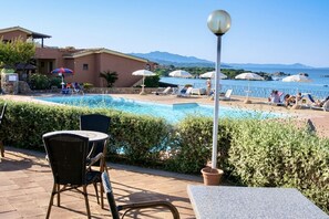 Zona de piscina con sillones de descanso, sombrillas y vista al mar.