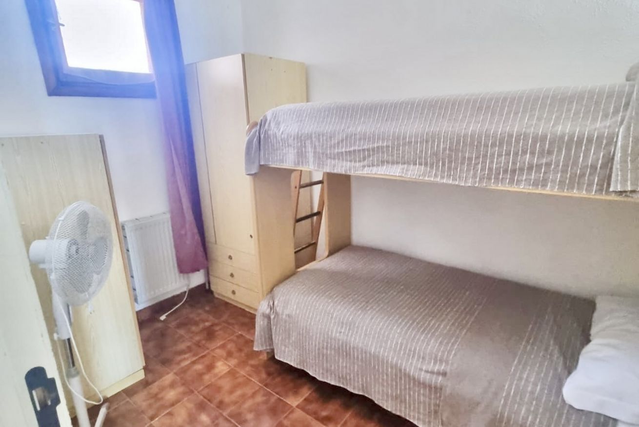 A dormitory room with bunk beds, a fan, a radiator, and a wardrobe.