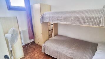 A dormitory room with bunk beds, a fan, a radiator, and a wardrobe.