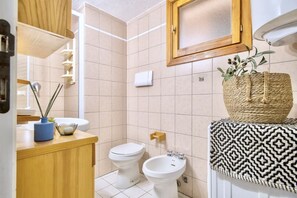 Baño con inodoro, bidé y lavamanos, armarios de madera y espejo.