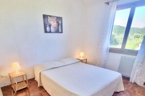 Un dormitorio con cama, lámparas de noche, un cuadro en la pared y ventana con vistas a zonas verdes.