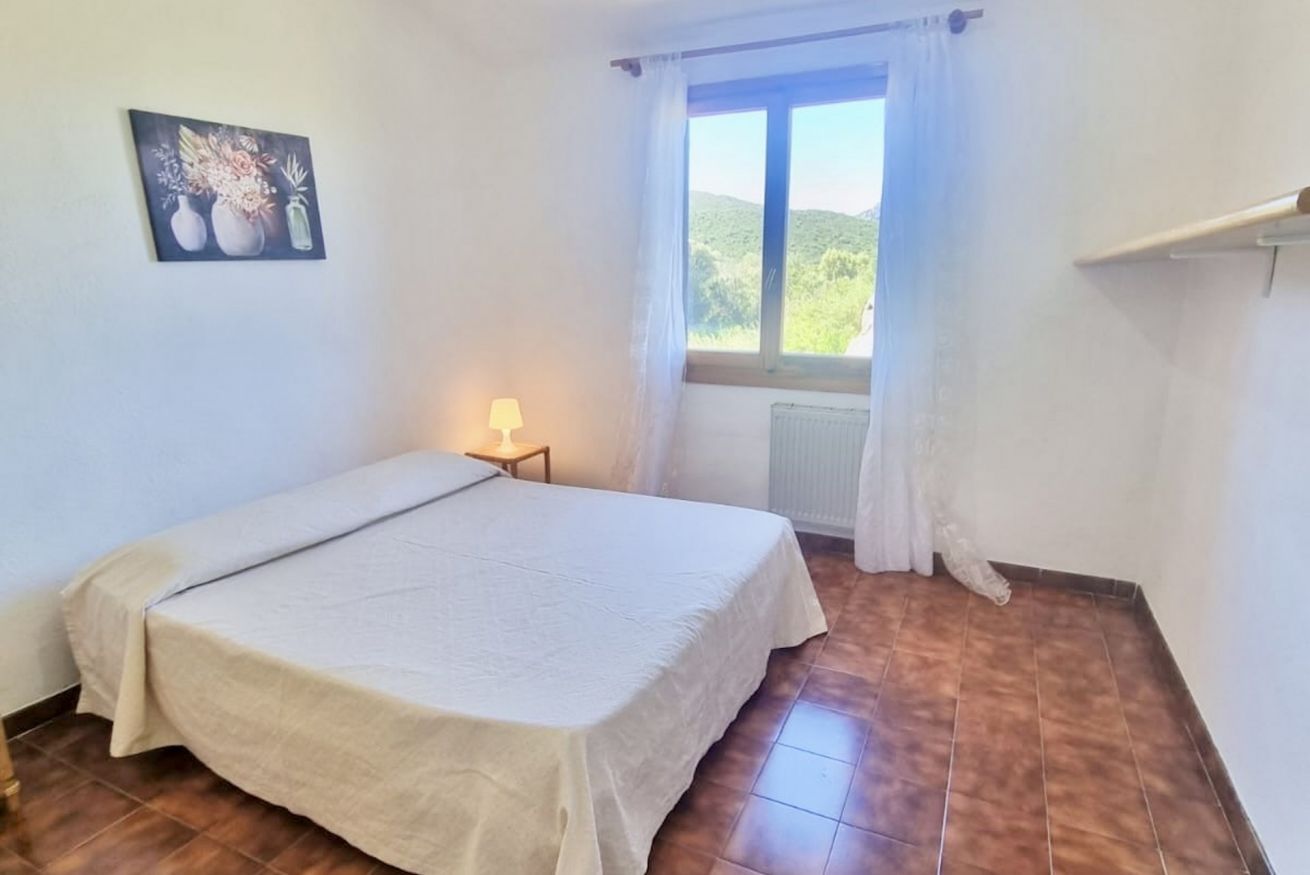A single-bed room with a window, a bedside lamp, and a painting on the wall.