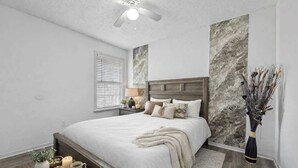 Een slaapkamer met een bed, nachtkastjes, een raam met jaloezieën en een wand met een marmerachtige textuur.