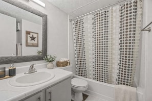Un bany amb un lavabo blanc, un vàter, una dutxera amb cortina de punts i un mirall amb un detall decoratiu d'estrella.