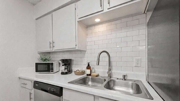 Een moderne keuken met witte kasten, een roestvrijstalen spoelbak, een magnetron en een vaatwasser.