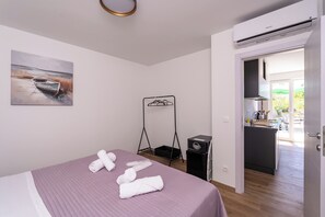 A bedroom with a bed, towels, a painting, a drying rack, and a view of the kitchen and balcony. - Romantic Leona Apartment with Large Terrace near Dubrovnik (Orašac)