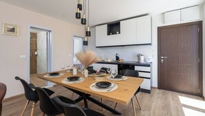 A modern dining area with a wooden table set for four, black chairs, and a hanging light fixture. - Romantic Leona Apartment with Large Terrace near Dubrovnik (Orašac)