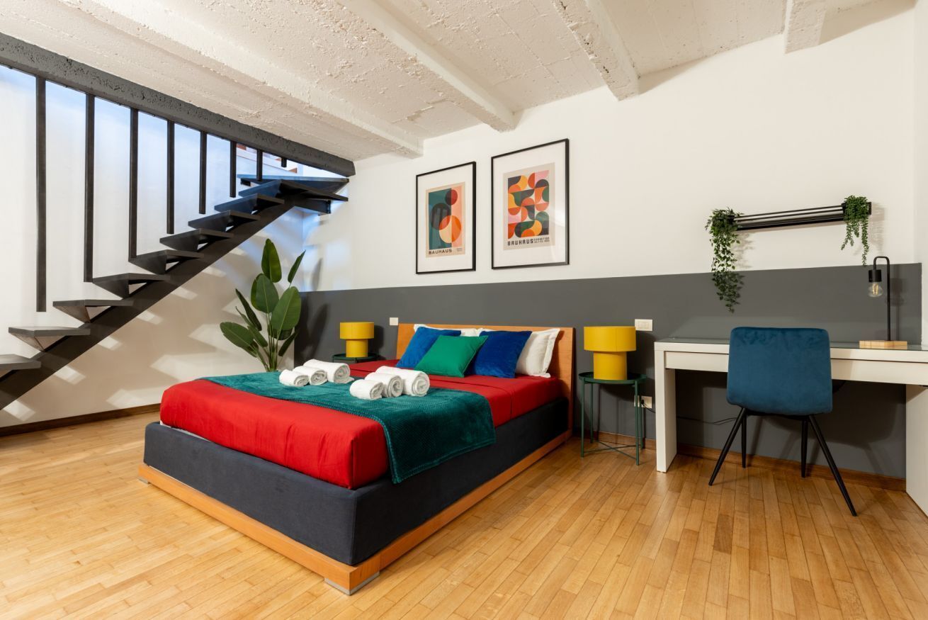 A modern bedroom with a bed, desk, chair, and a staircase.