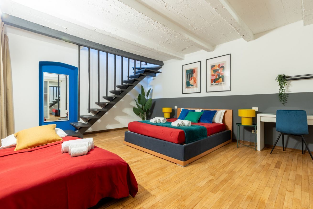 Un dormitorio moderno con cama, escritorio, silla, escalera y obras de arte en la pared.