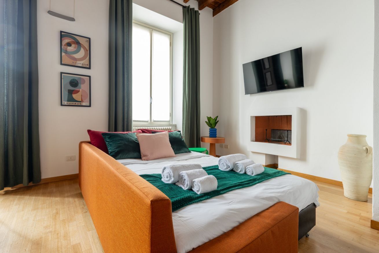 A modern hotel room with a bed, a flat-screen TV, a large vase, and artwork on the wall.