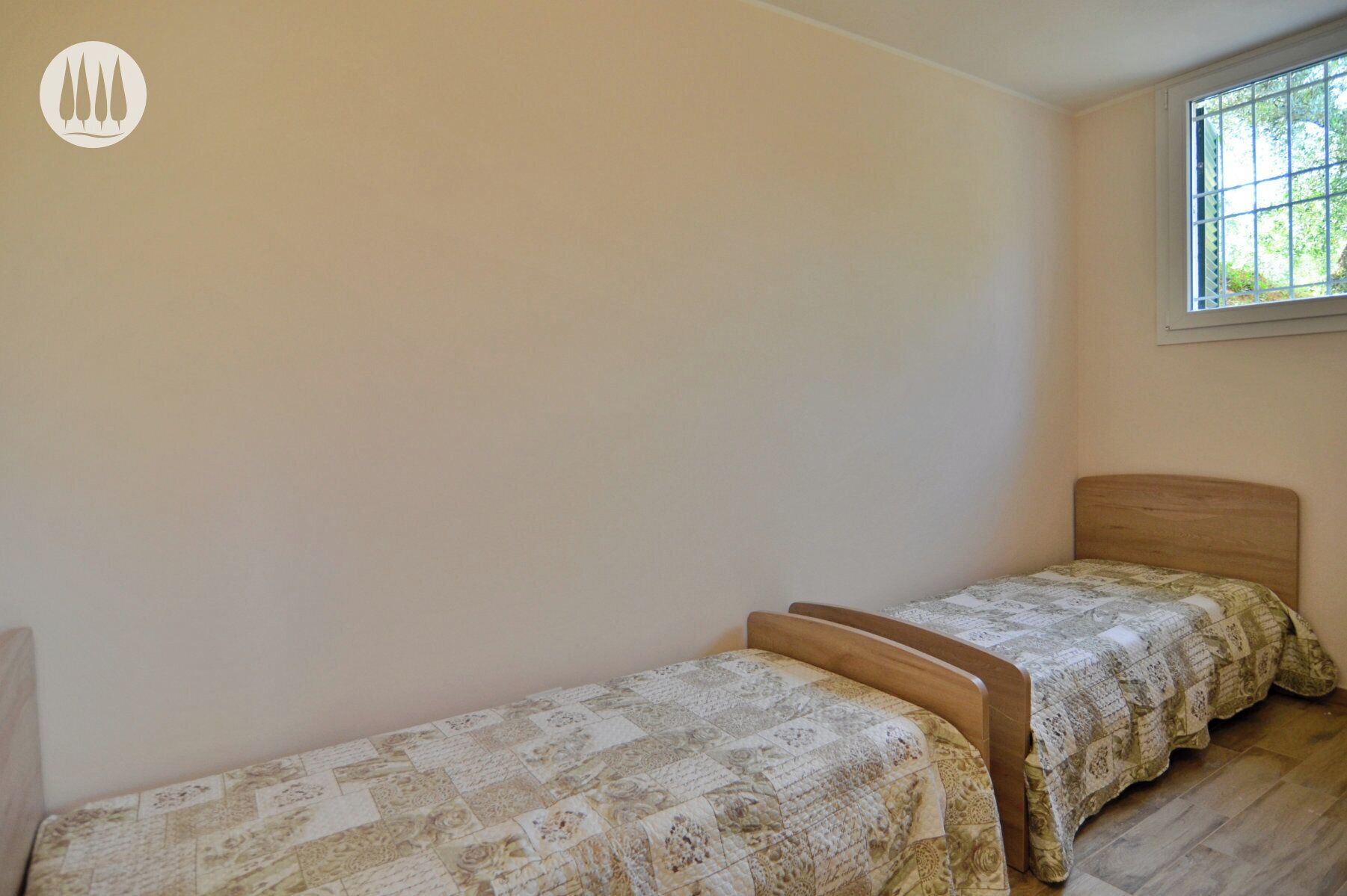 Una habitación pequeña y sencilla con dos camas individuales, una ventana y paredes sin decorar.