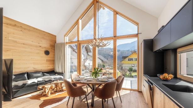 Une cuisine moderne dotée d’une grande fenêtre, un coin repas avec une table et des chaises en bois, et un espace salon confortable avec un canapé et une table basse.