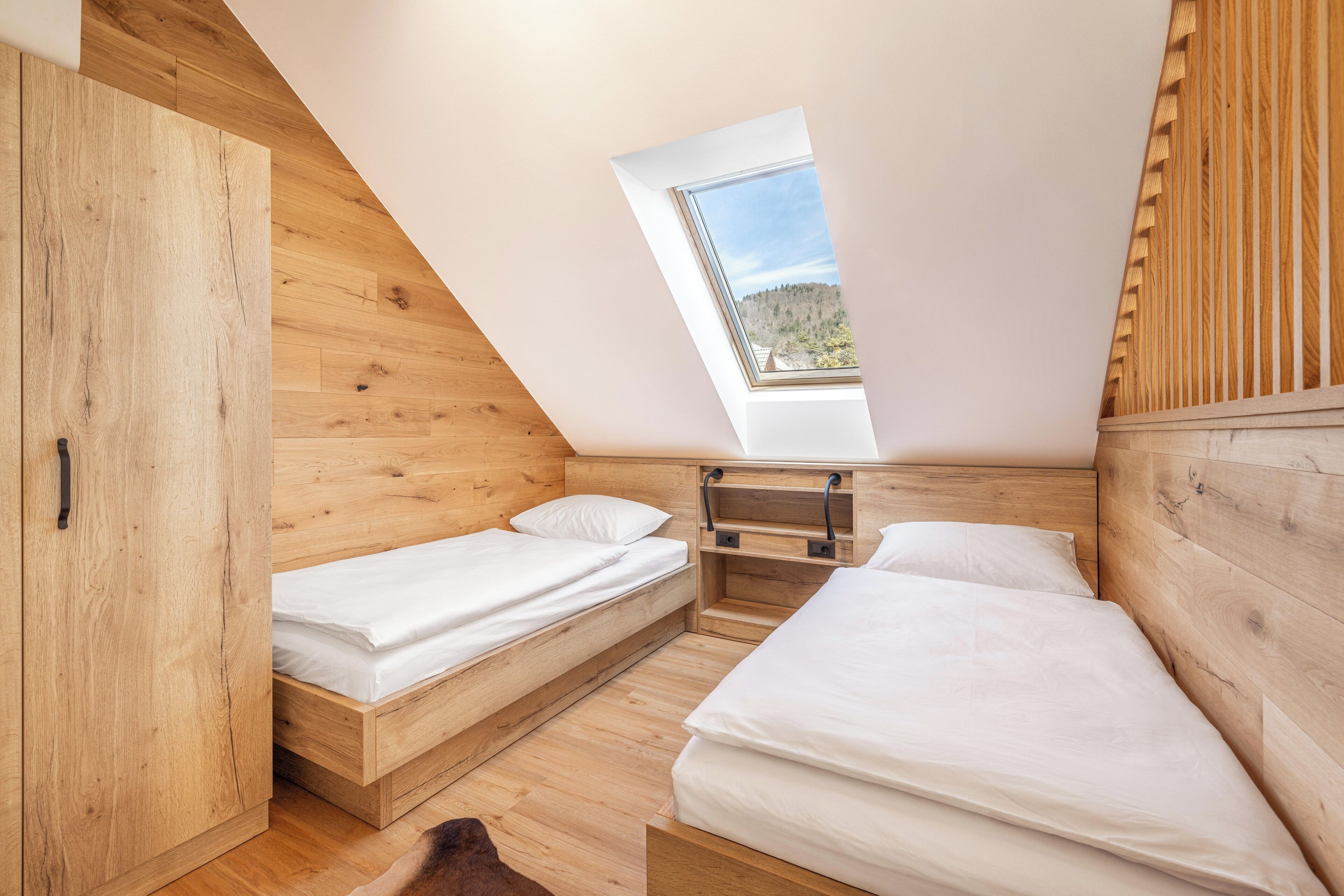 Une petite chambre à coucher en bois, avec deux lits, une lucarne et une armoire.