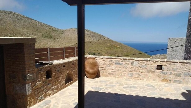 A stone terrace with a view of the sea, a large terracotta pot, and a wooden fence.