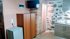 A compact kitchen with a stone wall, wooden cabinets, a built-in TV, and a small refrigerator.