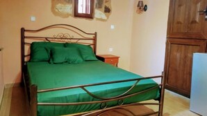 A single bed with a metal frame and green bedding in a room with a stone wall and a wooden door.