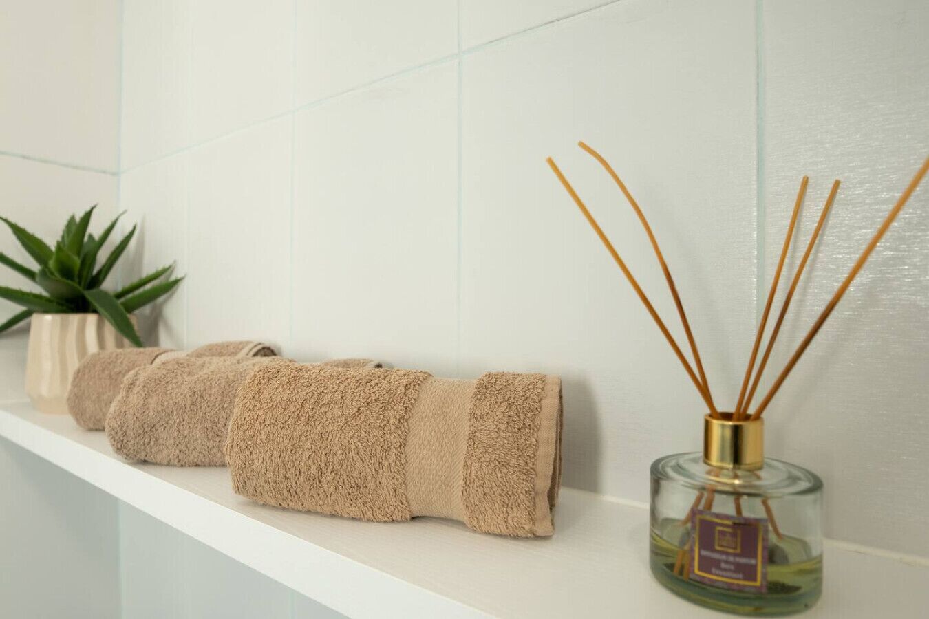 Une salle de bain avec une étagère blanche où sont rangées des serviettes pliées et un diffuseur de parfum à bâtonnets.