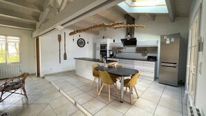 A modern kitchen with a central island, a dining table with chairs, a built-in oven, and a refrigerator. - 4* listed house located 6km from Boyardville beach and 3km from Dolus (Dolus d'Oléron)