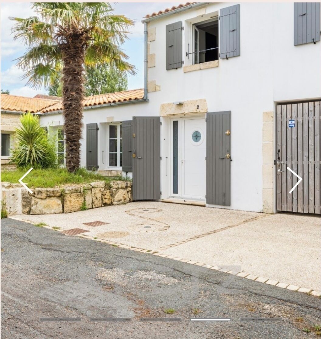 A two-story building with a white facade, grey shutters, and a stone wall.