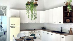 Una cocina moderna con armarios blancos, techo de madera y plantas colgantes.