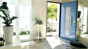 Ein Zimmer mit einem großen Fenster, einem Blumentopf, einem kleinen Tisch und einer Tür, die nach draußen führt.