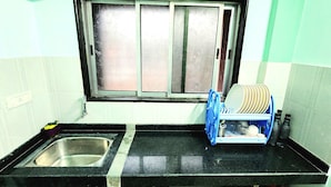 Una cocina con un lavamanos de acero inoxidable, un ventanal con vidrio esmerilado y un escurreplatos con platos.