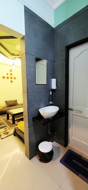 A bathroom with a white marble sink, a mirror, and a door. - The Purple Leaf (Economy) Home Stay – A Peaceful Family Retreat (Ratnagiri)