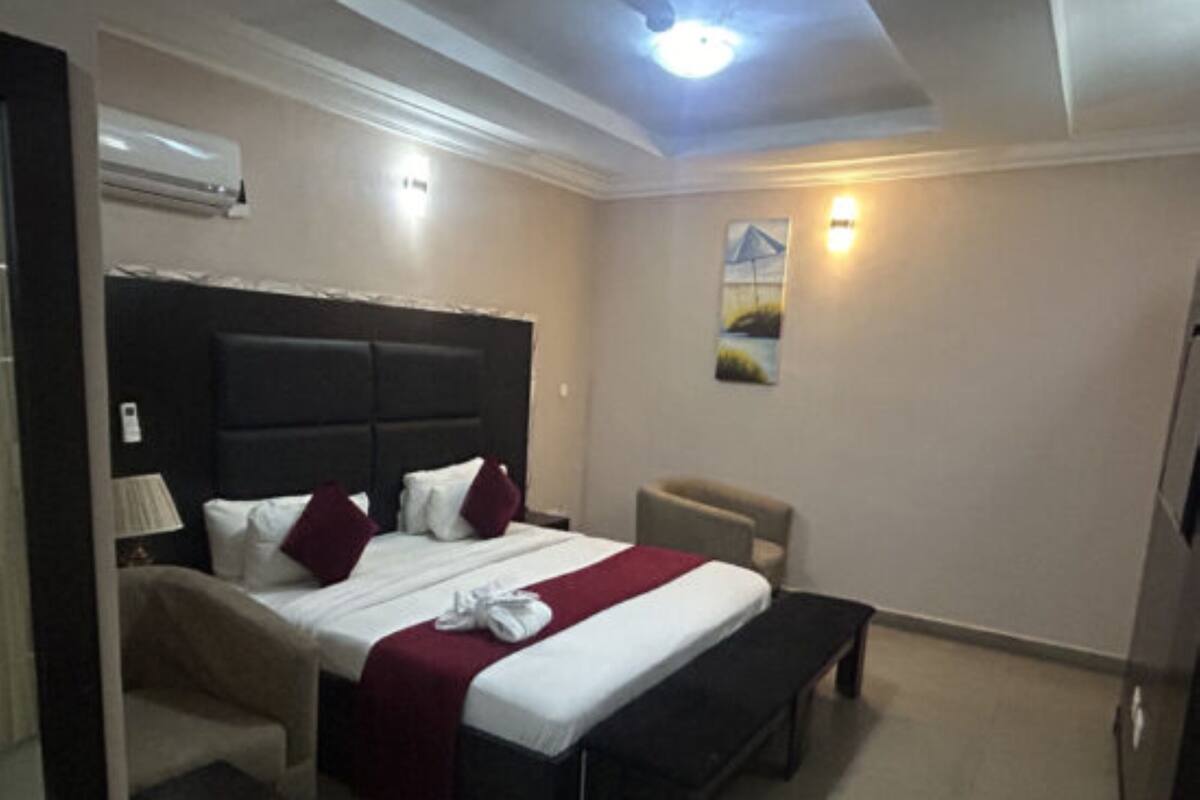 A hotel room with a bed, bedside table, chair, and a ceiling light.
