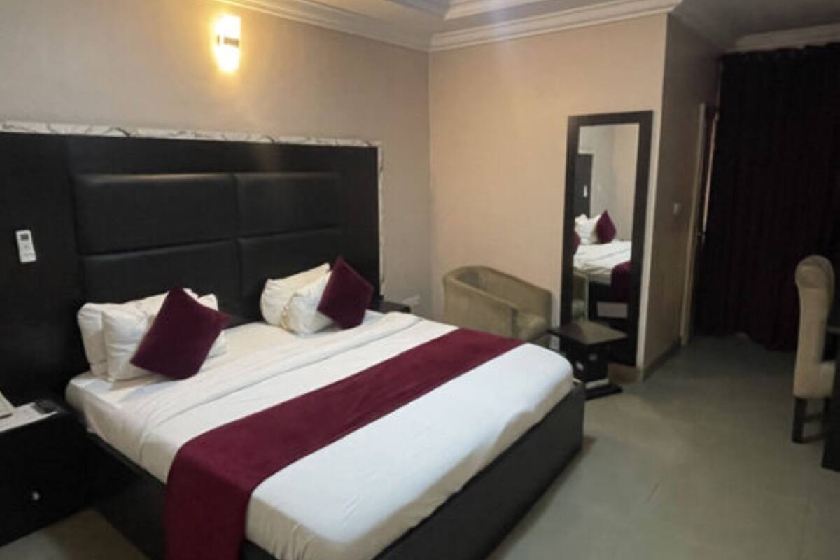 A hotel room with a large bed, a bedside table, a chair, a mirror, and a ceiling light.