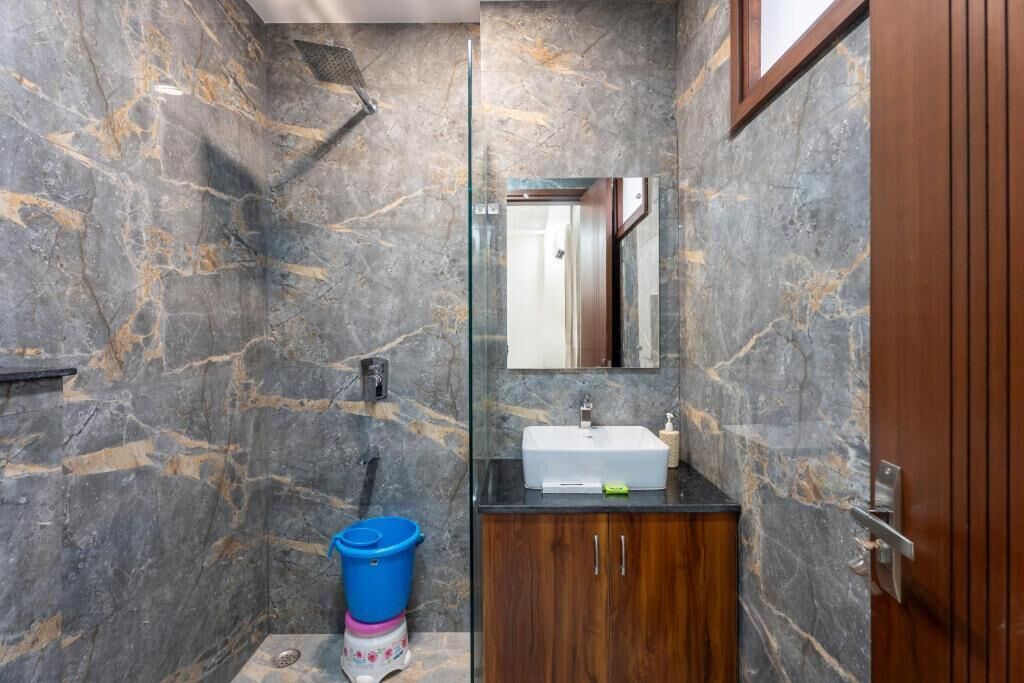 A bathroom with marble walls, a glass shower enclosure, a wooden cabinet, and a sink with a mirror above it.
