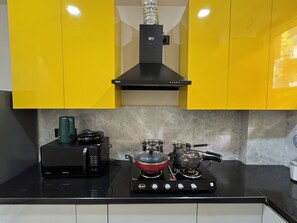Une cuisine avec des meubles de couleur jaune, une cuisinière noire et une bouilloire en acier inoxydable.